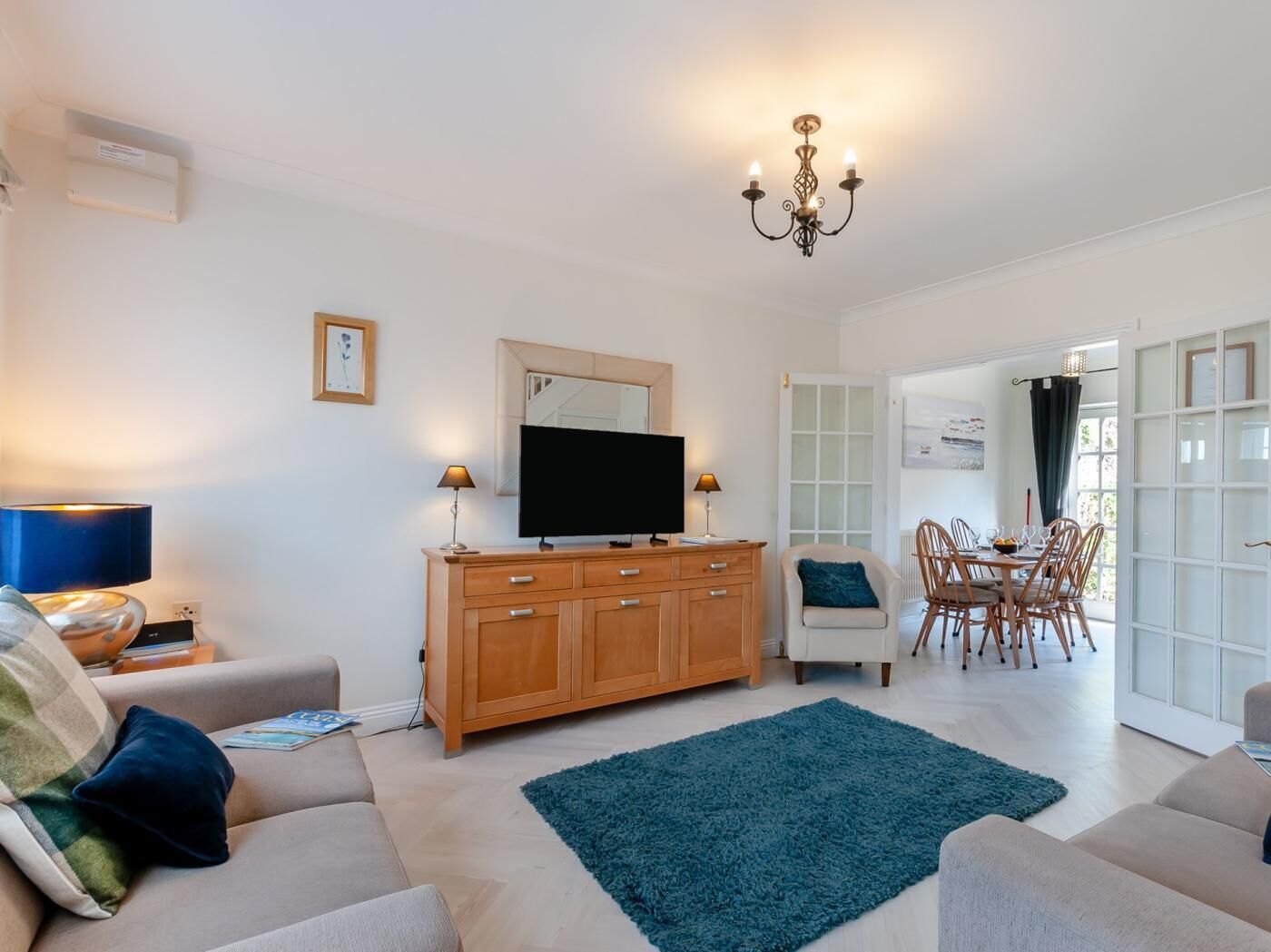 Un salon comprenant un téléviseur, un meuble en bois, deux canapés, un coin repas avec des chaises et un lustre.