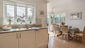 A kitchen with a large window, a dining area with wooden chairs, and a view of the backyard. - 4 Bed in Rye- (oc-bt104) (Rye)