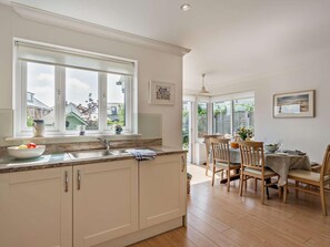 A kitchen with a large window, a dining area with wooden chairs, and a view of the backyard. - 4 Bed in Rye- (oc-bt104) (Rye)