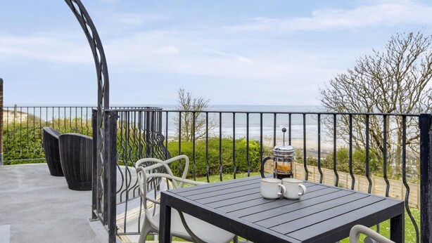 Un balcone con tavolo, sedie e barbecue, con vista sulla spiaggia.
