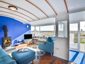 Ein modernes Wohnzimmer mit blauer Akzentwand, einem Kamin, einem Fernseher und einem großen Fenster mit Blick auf eine natürliche Landschaft.