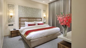 Une chambre d’hôtel avec un grand lit, des tables de chevet, une petite table, un vase avec des fleurs et un luminaire fixé au mur.