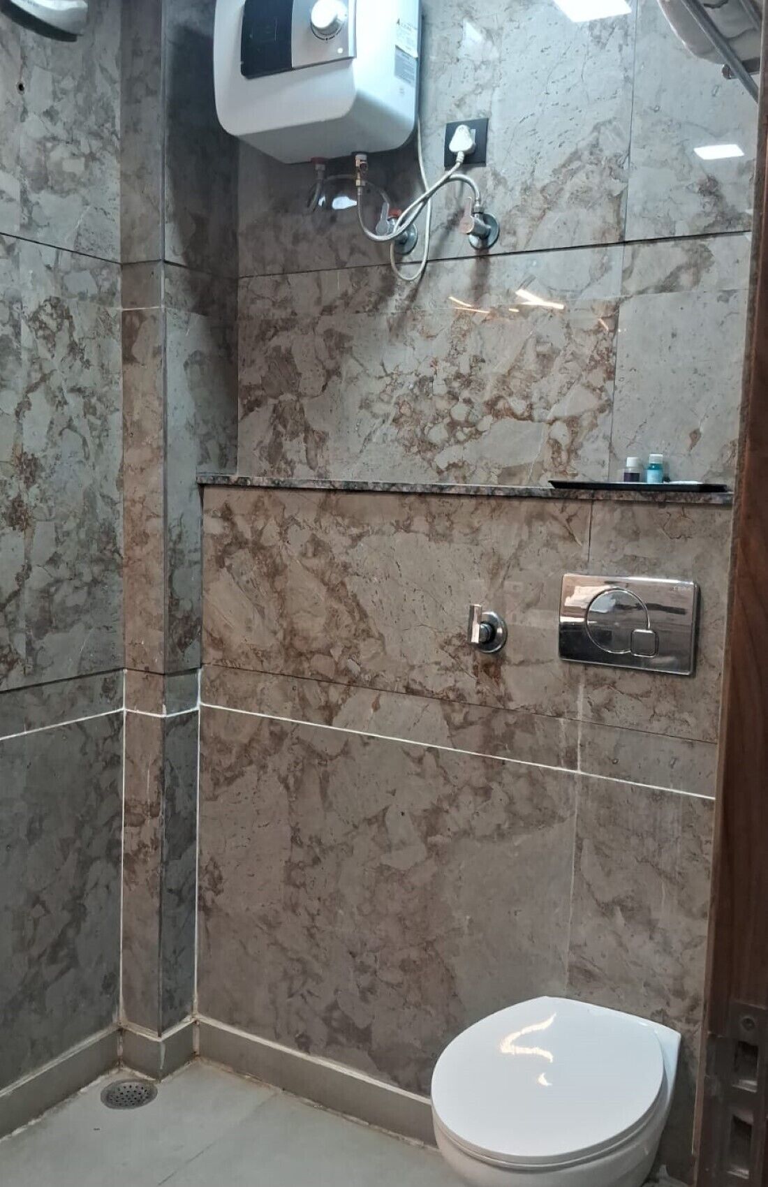 Un baño con inodoro, ducha y pared de mármol.