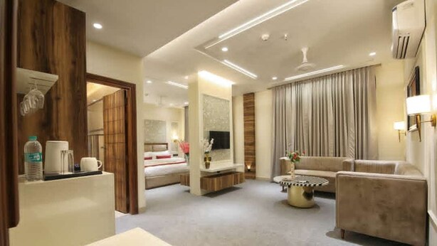 Une chambre d’hôtel moderne comprenant un lit, un coin salon avec un canapé et des fauteuils, une table basse et un téléviseur.