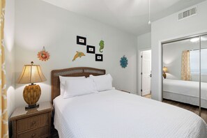 A neatly arranged bedroom with a bed, a nightstand, a lamp, and wall decorations including framed pictures and a mirror. - San Carlos 1808 by Liquid Life (Gulf Shores)