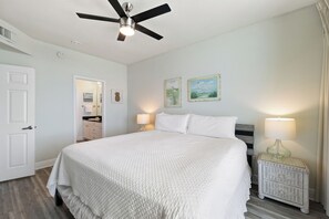 A bedroom with a bed, a nightstand, a lamp, a ceiling fan, and a door. - San Carlos 1808 by Liquid Life (Gulf Shores)
