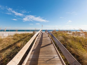 Ein Holzsteg führt zu einem Strand unter blauem Himmel.