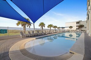A swimming pool with lounge chairs and palm trees, surrounded by a fence and a building. - San Carlos 1808 by Liquid Life (Gulf Shores)