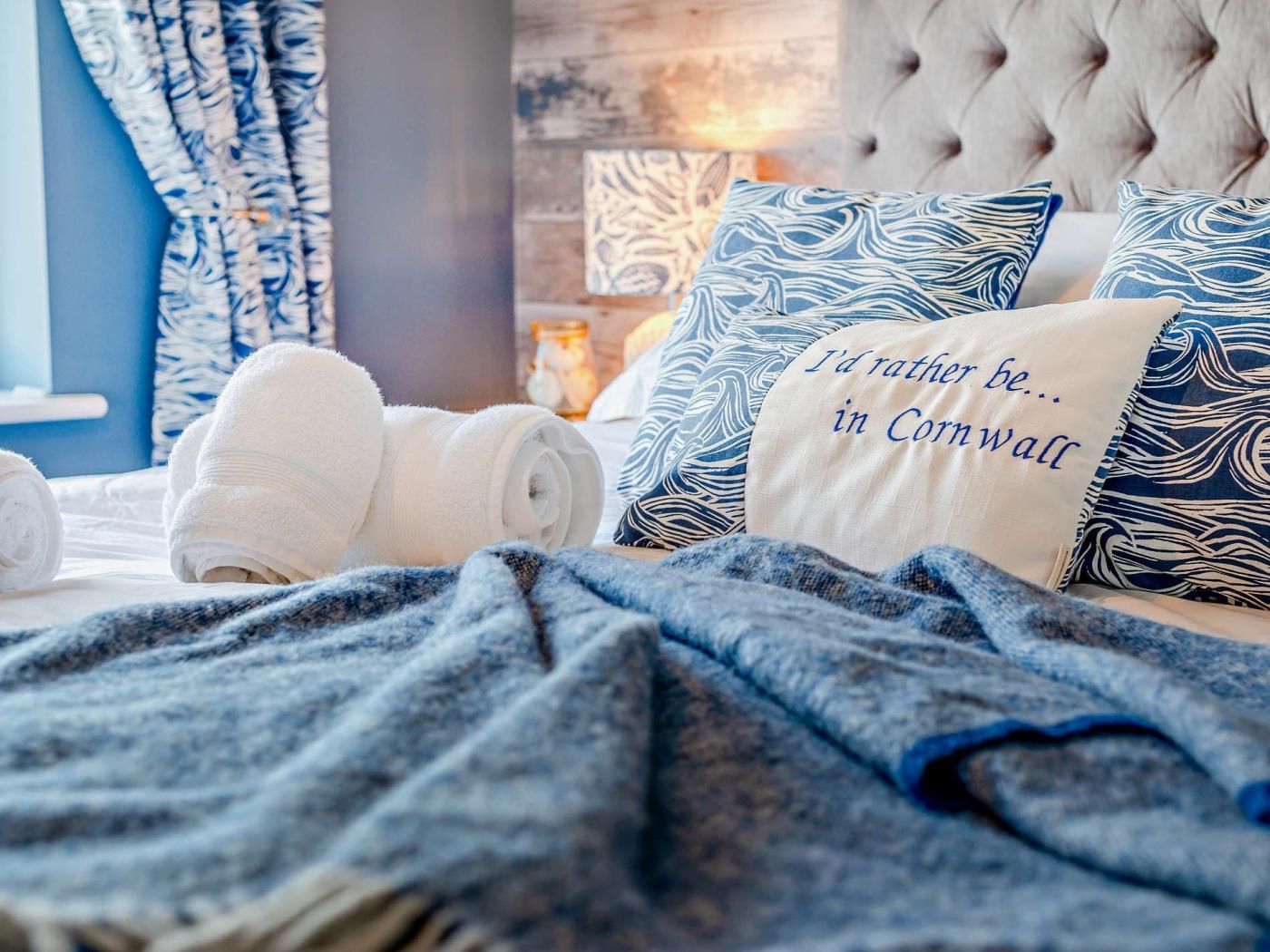 A neatly made bed with rolled white towels, a blue and white patterned pillow, and a pillow with text.