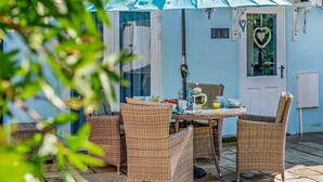 Un patio con mobiliario de mimbre, una mesa y un paraguas azul.