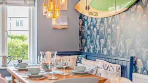 Un comedor con una mesa de madera preparada para dos personas, un frutero y una decoración de tabla de surf en la pared.