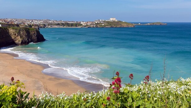 Vista costera con una playa arenosa, mar azul cristalino y un pueblo al fondo.