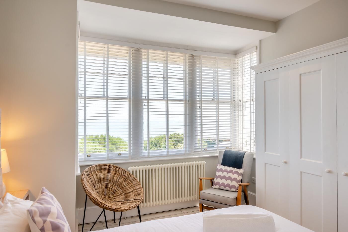A bedroom with a bed, a chair, a radiator, and a window with blinds.