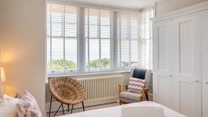 Ein Schlafzimmer mit Bett, Sessel, Heizkörper und einem Fenster mit Jalousien.