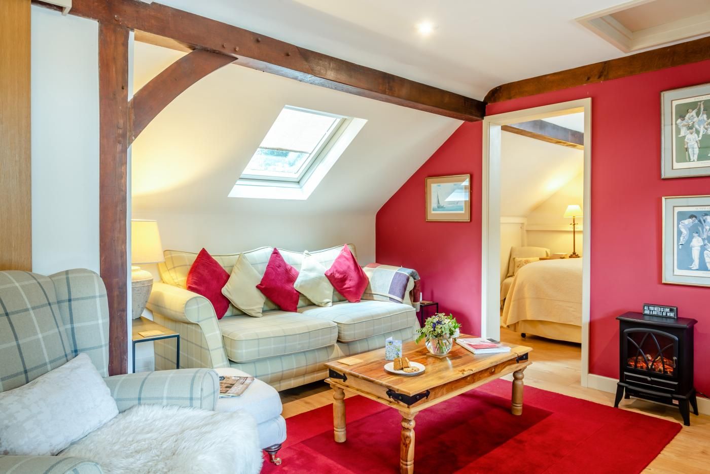 A cozy room with a sloped ceiling, a sofa with colorful cushions, a wooden coffee table, and a red carpet.