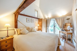 Ein Schlafzimmer mit einem großen Bett, einem Holzkopfteil, Nachttischlampen, einem Schreibtisch mit Spiegel und einem Fenster mit Vorhängen.