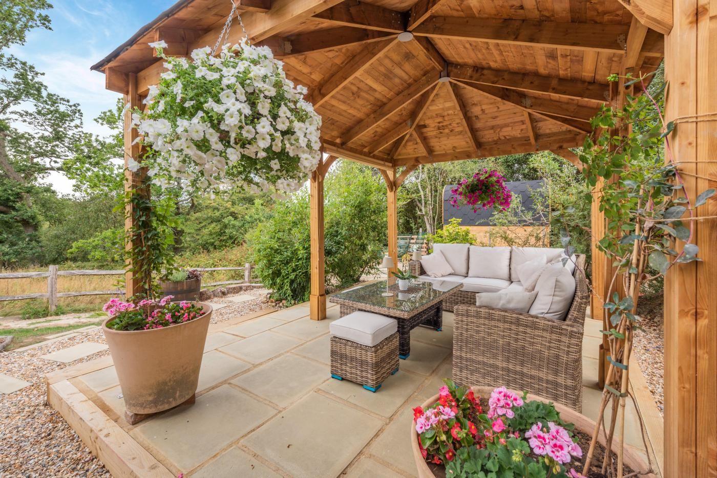 A covered outdoor seating area with a glass-top table, wicker furniture, and potted plants.