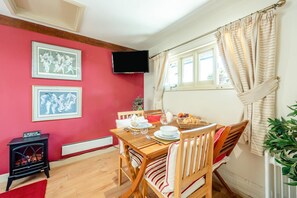 A dining area with a table set for two, a television mounted on the wall, and a red wall with framed pictures. - 1 Bed in Battle (oc-bt112) (Battle)