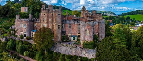 Un edificio parecido a un castillo con múltiples torres, rodeado de exuberante vegetación y un cielo despejado.