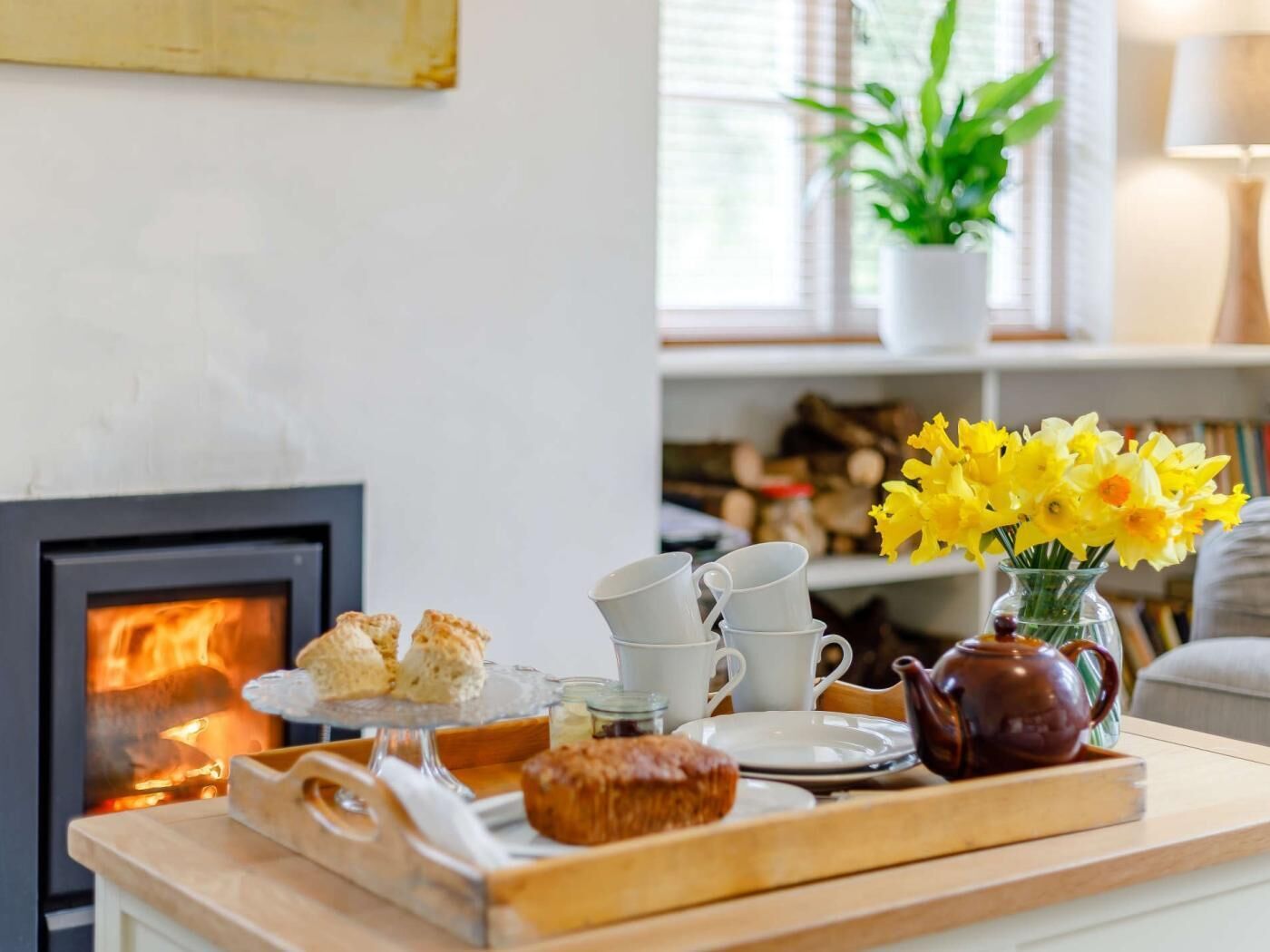 Een gezellige woonkamer met een open haard, een dienblad met gebak, een theepot en een vaas met bloemen.