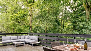 Eine Holzterrasse mit einer Couch, Korbstühlen, einem Tisch mit Speisen und Getränken und einem Holzzaun.