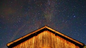 Eine Holz-Blockhütte, durch das Fenster ist ein Sternenhimmel zu sehen.