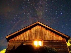 Eine Holz-Blockhütte, durch das Fenster ist ein Sternenhimmel zu sehen.
