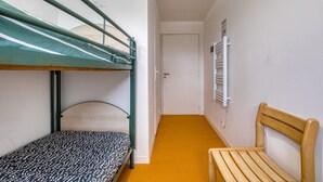 A dormitory room with bunk beds, a wooden bench, a radiator, and a door.
