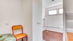 A small, single-room apartment with a bed, a chair, a shower area, and a window. - Room with Shared Terrace and Wi-Fi, 10 Minutes from the Beach (Mudaison)