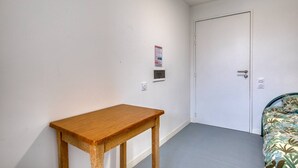 A room with a wooden table, a bed with a patterned bedspread, a white door, and a wall-mounted thermostat. - Room with Shared Terrace and Wi-Fi, 10 Minutes from the Beach (Mudaison)