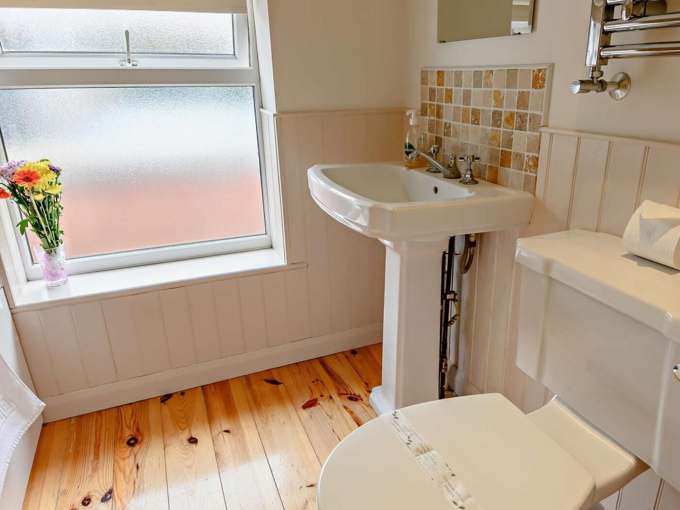 Un baño con ventana, lavamanos, inodoro y espejo.
