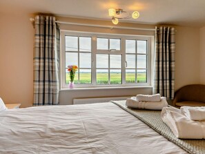 Ein Schlafzimmer mit einem großen Bett, einem Fenster mit Blick auf Felder und einem Nachttisch mit Blumen in einer Vase.