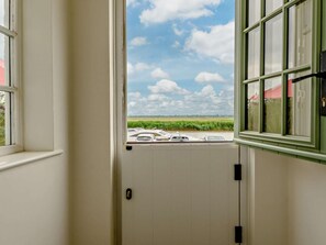 Blick durch eine Tür mit Fenster auf einen Parkplatz mit Autos und ein grünes Feld unter teilweise bewölktem Himmel.