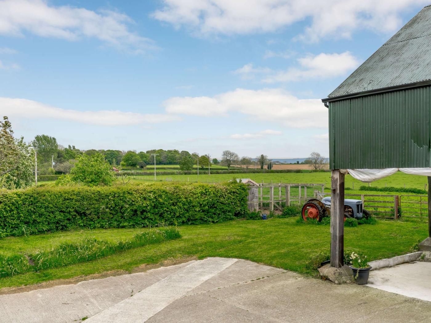 A rural landscape with a green barn, a tractor, and a clear sky.