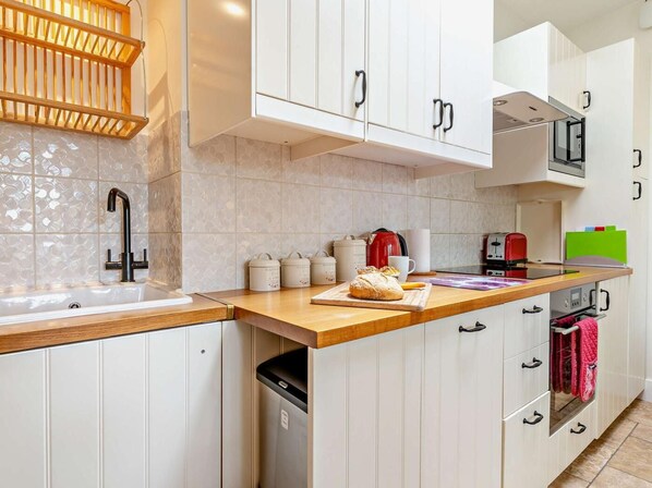 A modern kitchen with white cabinets, a wooden countertop, a built-in oven, and a stainless steel sink.