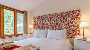 Habitación de hotel con cama, dos mesitas de noche, una ventana y un cabecero estampado con motivos florales.