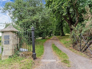 A gravel path leading through a wooded area with a stone structure and metal gate.