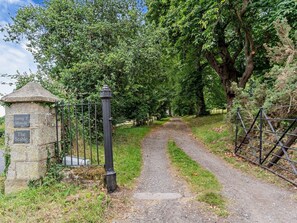 A gravel path leading through a wooded area with a stone structure and metal gate. - 1 Bed in Abergavenny (oc-47886) (Pantygelli)