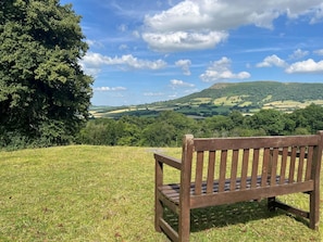 A wooden bench on a grassy hill overlooking a hilly landscape with trees and a clear sky.