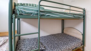 Ein Etagenbett mit grünem Metallgestell, eine untere Schlafstelle mit gemustertem Bett und ein Einzelbett mit Holz Kopfteil.