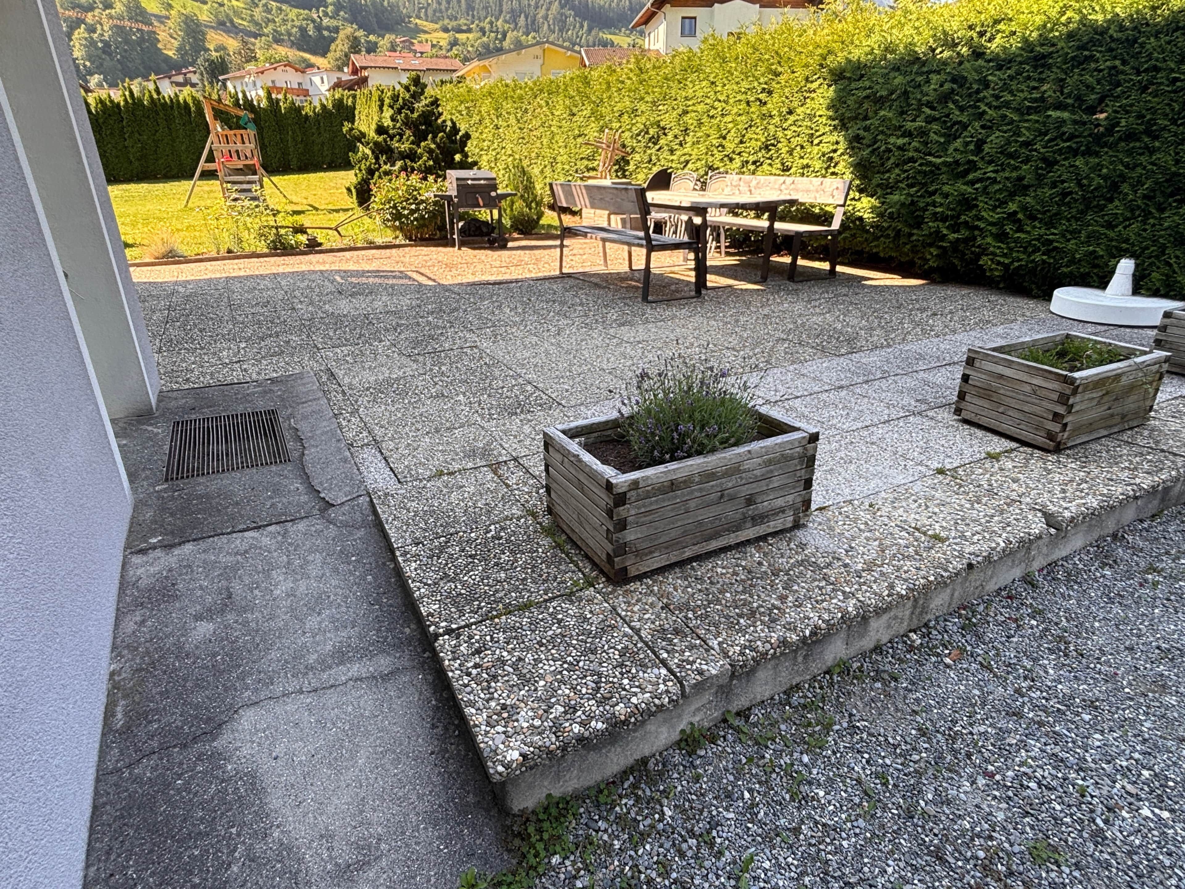 Eine Terrasse mit Kiesbelag, Holz-Pflanzkästen und einer Sitzbank.