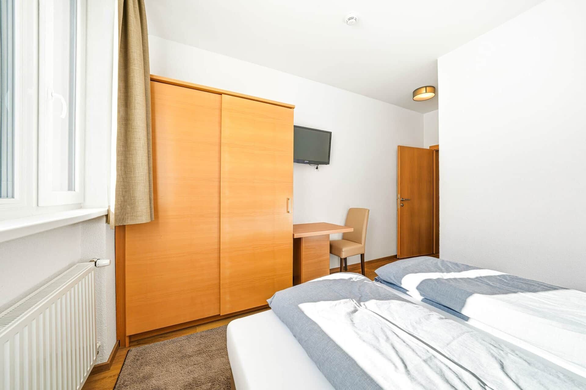 Quarto com cama, escrivaninha, cadeira, guarda-roupa e televisão.
