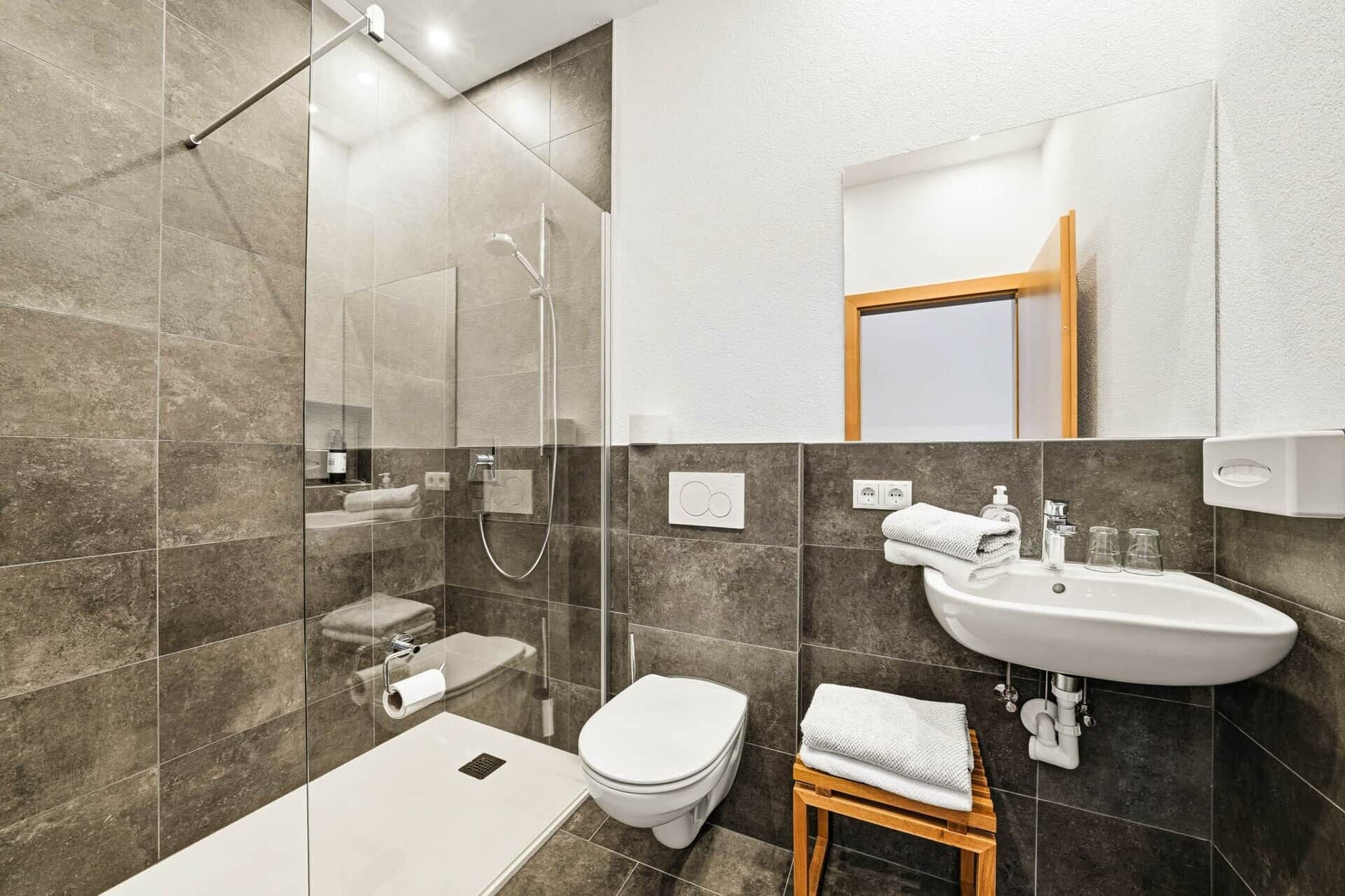 Ein modernes Badezimmer mit Dusche, Toilette, Waschbecken und einem kleinen Holzschemel.