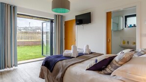 Une chambre d’hôtel comprenant un lit, une télévision, une salle de bain avec un lavabo et une porte-fenêtre coulissante donnant sur un jardin.
