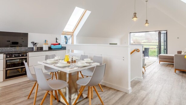 Une cuisine moderne avec un coin repas, une chambre à coucher aménagée en mezzanine avec une lucarne et une vue sur l’extérieur.