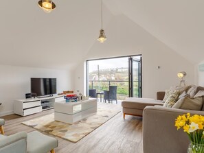 Ein modernes Wohnzimmer mit Fernseher, einem Glastisch, einer Couch und Blick durch große Fenster.