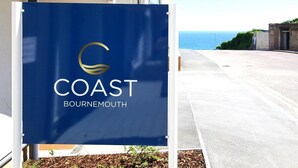 Schild für 'COAST Bournemouth' mit Logo, in einem Parkbereich mit Blick auf das Meer.