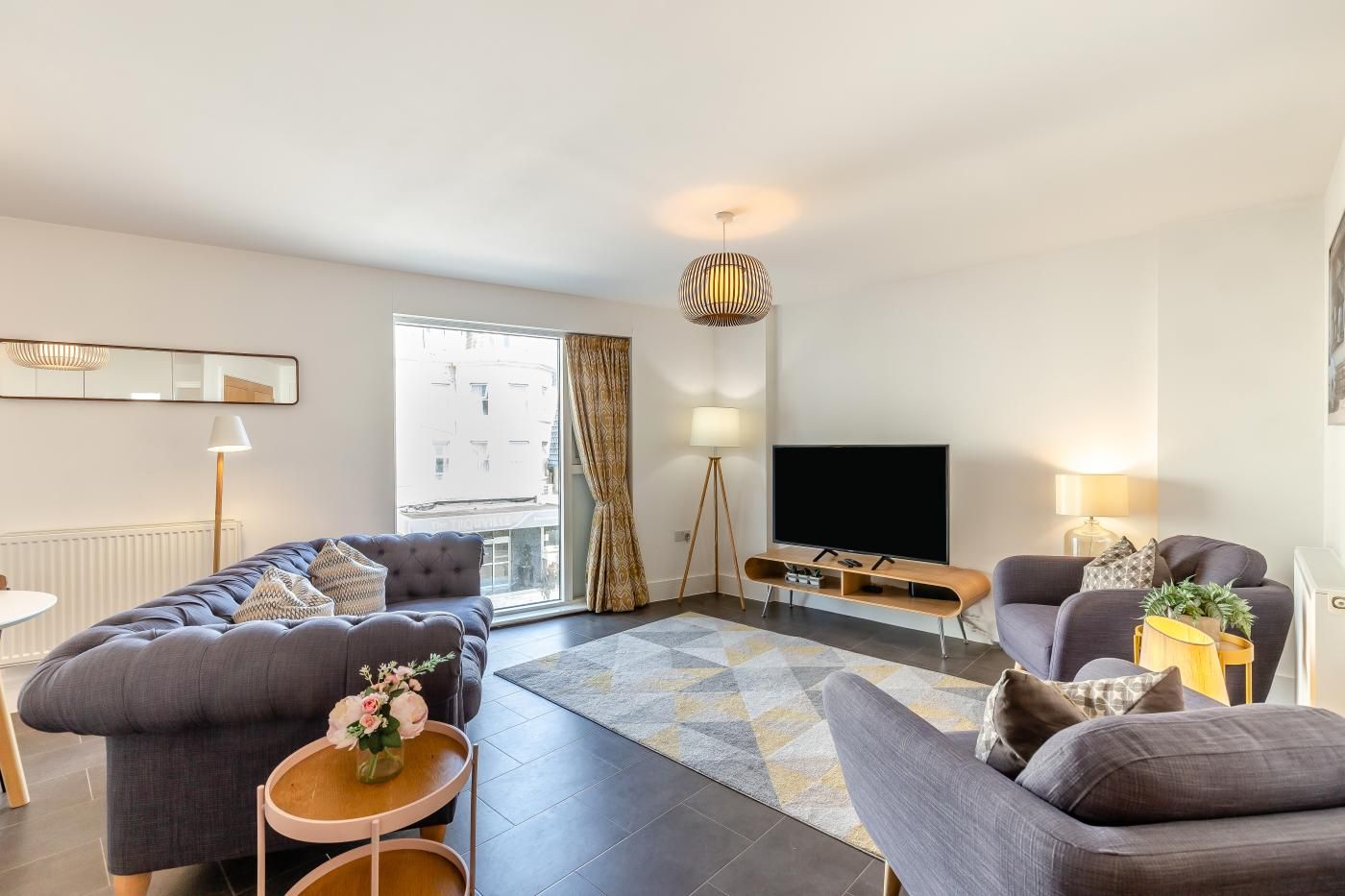 Ein modernes Wohnzimmer mit einer Sofagarnitur, einem Flachbildfernseher und einer Stehlampe.