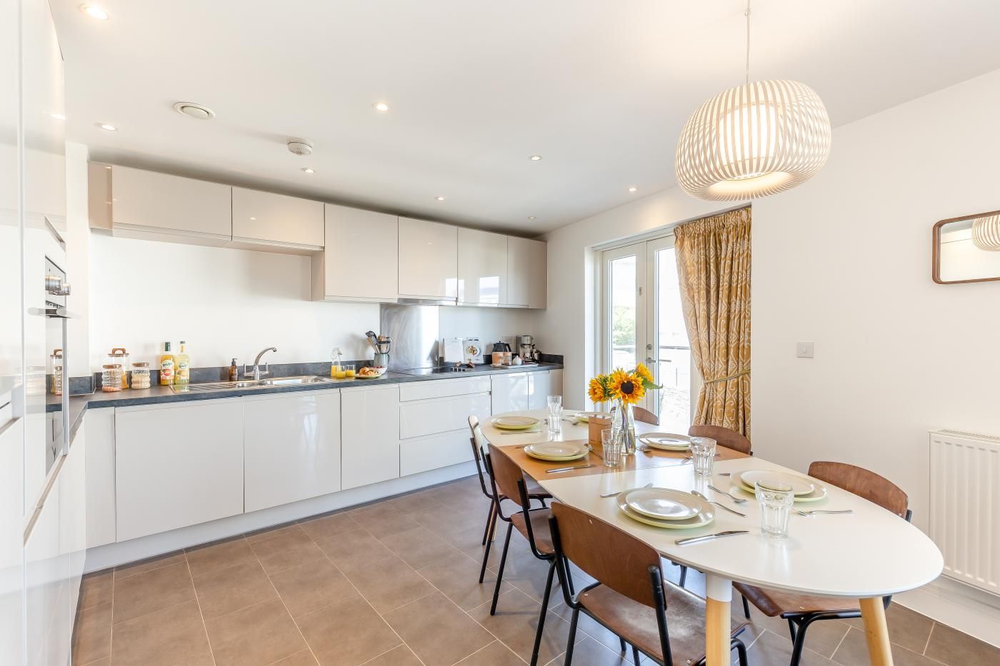 A modern kitchen with white cabinets, a dining area with a round table set for four, and a large window with curtains.