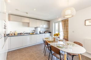 A modern kitchen with white cabinets, a dining area with a round table set for four, and a large window with curtains. - 2 Bed in Bournemouth (oc-48516) (Bournemouth)